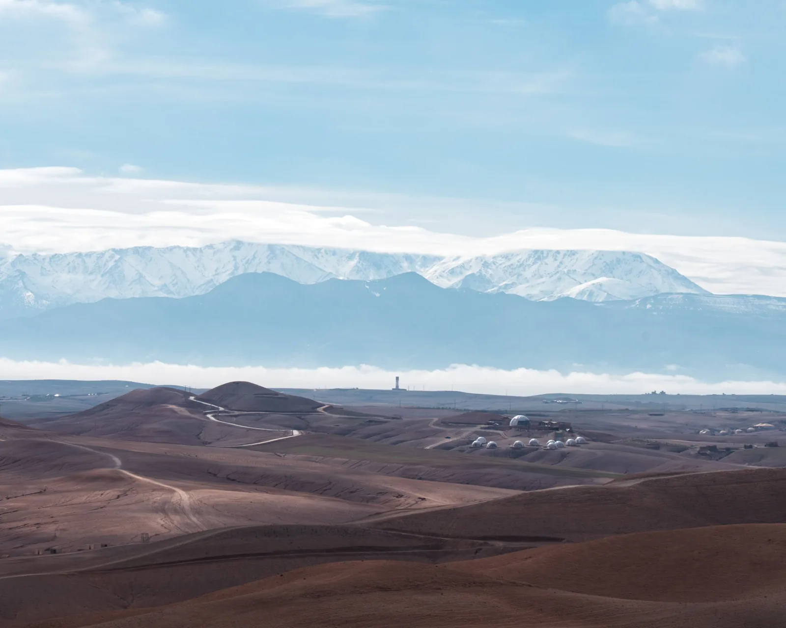 Dome camp among Agafay hills with snow-covered Atlas Mountains beyond