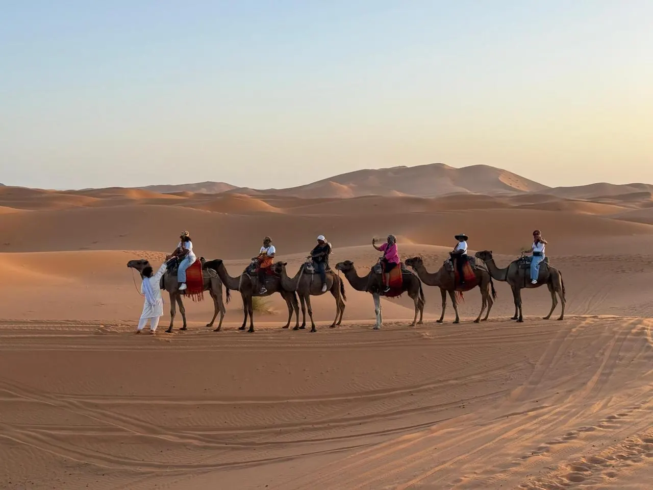 Guide leading travelers on camels across the Erg Chebbi dunes