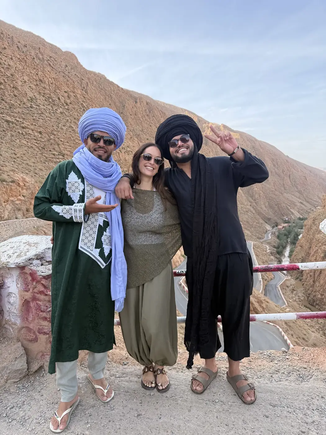 Viajero posando con dos guías sobre la carretera sinuosa de la garganta del Dades