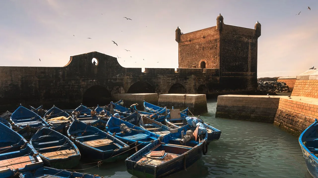 Blue fishing boats beside the stone harbor tower in Essaouira