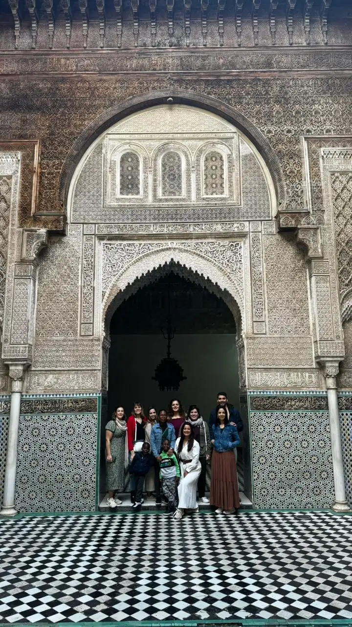 Travelers beside a decorated arch and tiled courtyard in Fes