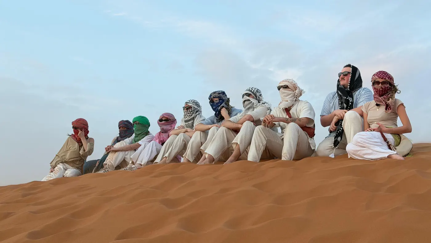 Viajeros con pañuelos de colores sentados juntos en la cresta de una duna de Erg Chebbi
