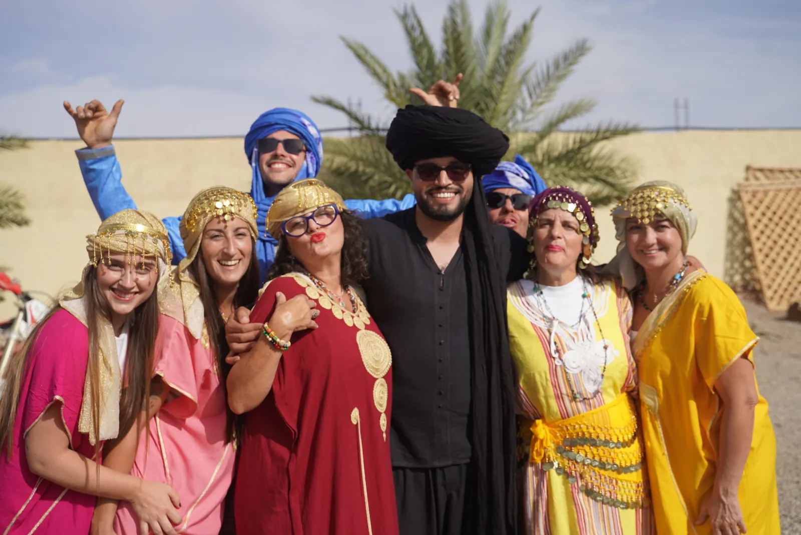 Viajeros con vestimenta tradicional de colores posando con un guía cerca de una palmera